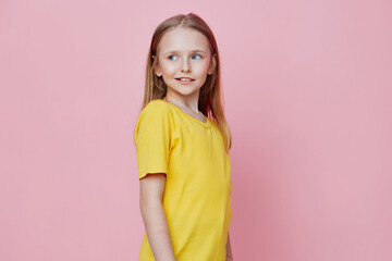 Smiling girl in a bright yellow shirt against a pastel pink background, showcasing youthful joy and playful innocence, ideal for children s fashion and lifestyle concepts
