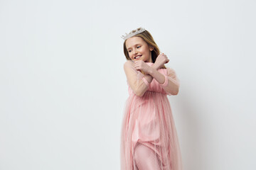 A joyful young girl in a pink tulle dress and tiara, crossing her arms with a smile against a...