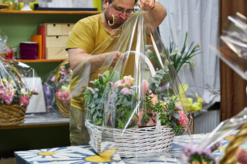 a male florist in a yellow T-shirt packs a large basket of flowers in the workshop