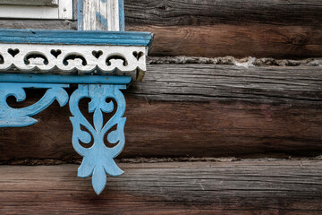 Detail of ornate window frame. Corner of decorative window frame. Details of window framing of log house close-up. Window on wall framed with carved elements in white and blue.