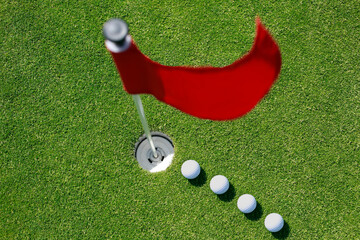 Close up of line of golf balls on green with red flag.