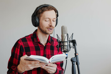 Young man narrator recording audiobook using microphone at recording studio.