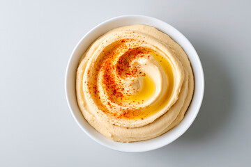 Classic hummus with olive oil and paprika served in white bowl on light grey background