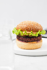 Vegetarian Burger made with vegan cutlet, burger bun, salad, cucumber, cheddar cheese and onion on a light concrete background. Delicious vegan food