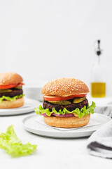 Vegetarian Burger made with vegan cutlet, burger bun, salad, cucumber, cheddar cheese and onion on a light concrete background. Delicious vegan food