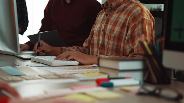 A vibrant workspace scene showing individuals engaged in collaborative work at computers, with items scattered around, including books, stationery, and creative tools. SACTR
