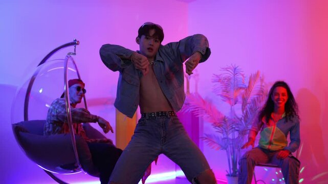 Skilled asian dancer moving to modern music while multicultural friend sitting at chair. Professional performer dancing show energetic foot step while hipster team cheering and supporting. Regalement.