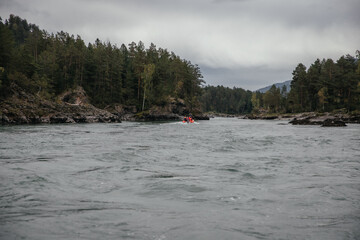 Group of people in a raft navigating a scenic river surrounded by lush forest. The overcast sky...