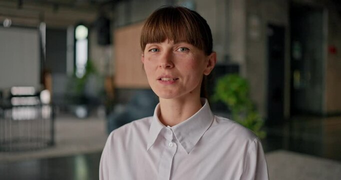Portrait of confident businesswoman in a white shirt sitting on a gray carpet posing, during the workday and looking directly at the camera in the office