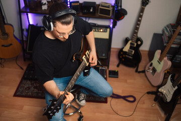 A guitarist sits on a stool in a home studio, playing a black Les Paul electric guitar. A vibrant...