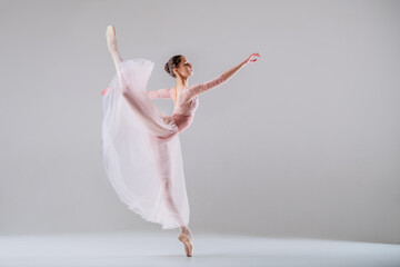 young slender ballerina in pointe shoes and a pink leotard dances on a white background