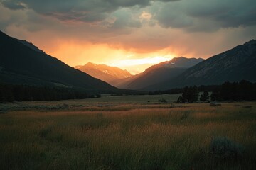Obraz premium Mountain valley with meadow at sunset; dramatic sky with orange and grey clouds.