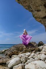 Woman, seashore, rocks: Woman with pink fabric poses on rocky seashore under sunny sky during photoshoot.