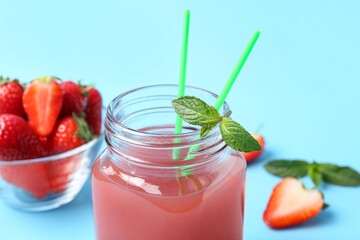 Mason jar of juice and bowl with strawberry on blue background