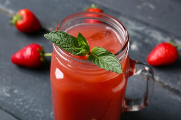 Mason jar of tasty strawberry juice on black wooden table