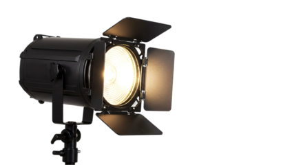 A black fresnel light with barn doors on a stand against a black background shining brightly light