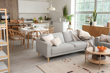 Interior of light open space kitchen with cozy grey sofa and oranges on wooden coffee table