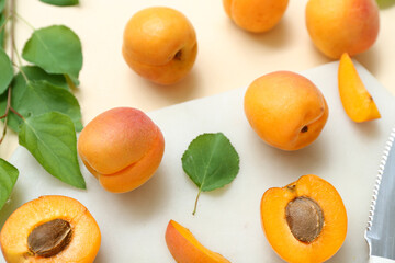 Board with fresh apricots and leaves on beige background