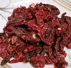 A vibrant pile of Kashmiri dry red chilies with deep red color and wrinkled texture, served on a patterned plate. Known for mild heat and rich color in Indian curries and spice blends.