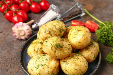 Plate of boiled baby potatoes with dill and tomatoes on dark background