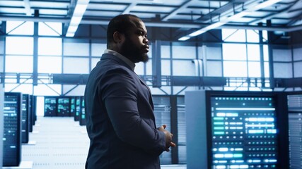 African american technician walking in data center, monitoring systems to identify errors. Man in...