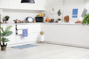 Interior of modern kitchen with stylish rug, trash bin and white counters