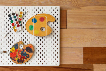 Pegboard with paints and palettes on wooden wall