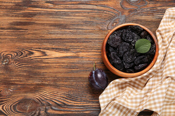 Bowl with tasty dried plums on wooden background