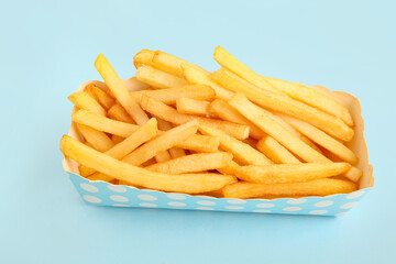 Paper box with tasty french fries on blue background