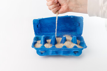 DIY underwater-themed craft in progress, hand adding sand to blue egg carton. Recycled material project for kids. sustainability campaigns, craft suppliers, parenting blogs.