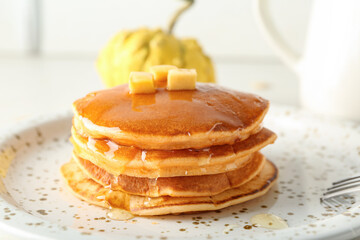 Plate of tasty pumpkin pancakes with honey and pieces of butter on white background
