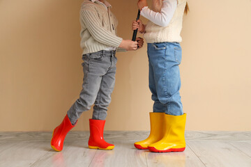 Little children in rubber boots with umbrella near beige wall