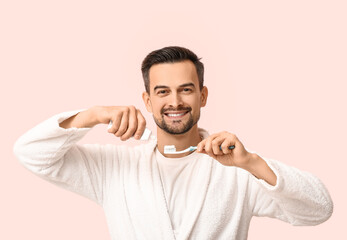 Handsome man squeezing tooth paste onto brush on pink background