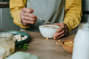 Man eating yogurt with granola in bowl on wooden table