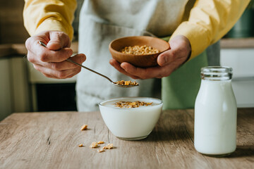 Close up of man adding granola to yogurt bowl