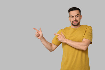 Handsome worried young man pointing at something on grey background