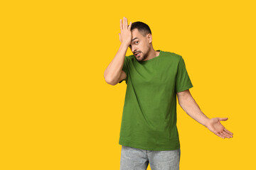 Handsome ashamed young man covering face with hand on yellow background
