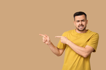 Handsome ashamed young man pointing at something on brown background