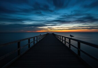 Obraz premium A wooden pier stretches out into the ocean as the sun sets, seagulls perched on the railings.