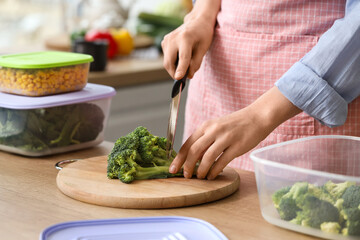 Woman cutting broccoli for freezing on wooden table in kitchen, closeup