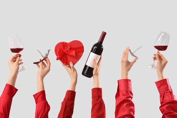 Women with red wine, gift and corkscrews on light background. Valentine's Day celebration