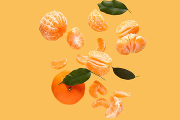 Flying sweet ripe mandarins and leaves on yellow background