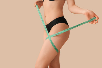 Young woman measuring her leg on brown background. Weight loss concept