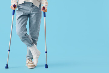 Injured young woman after accident with crutches on blue background