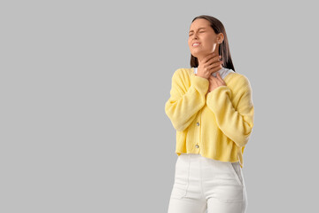 Young woman suffering from sore throat on grey background
