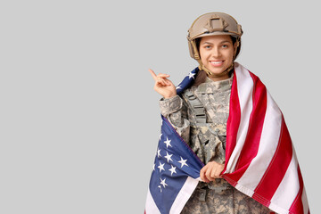 Female soldier with USA flag pointing at something on grey background