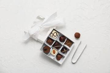 Box with candies and kitchen tongs on light background