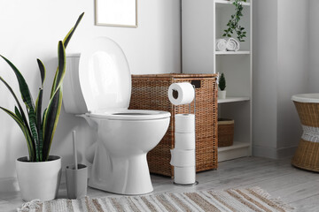 Toilet bowl, laundry basket, paper holder and houseplant in restroom