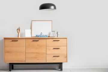 Commode with blank frames, decor and pendant lamp near light wall in room