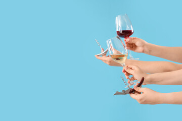 Female hands holding glasses of wine and corkscrews on blue background